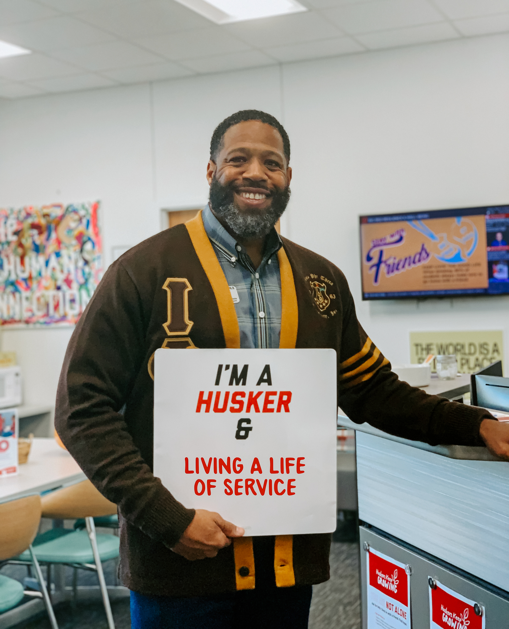 Kenji smiles for a photo with a sign that says "I'm a Husker & living a life of service"
