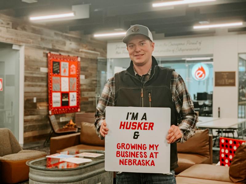 Carter smiles for a photo with a sign that says “I’m a Husker & growing my business at Nebraska”