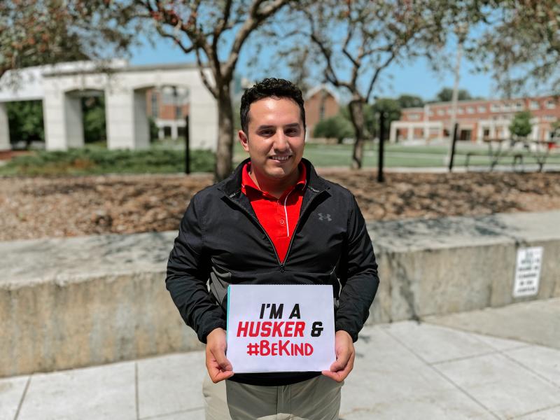 Cesar smiles holding a sign that says "I'm a Husker & #BeKind"