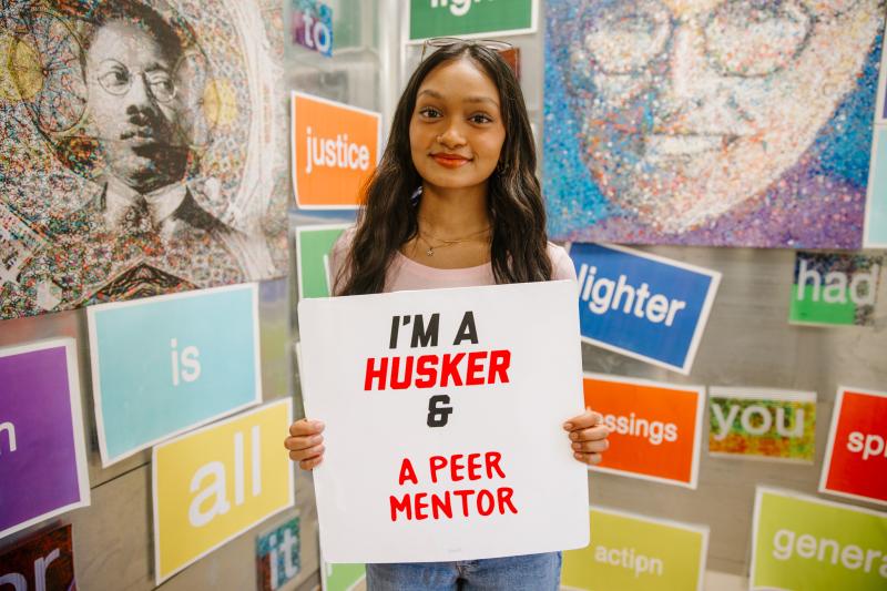 Dinushi smiles for a photo with a sign that says "I'm a Husker & a peer mentor"