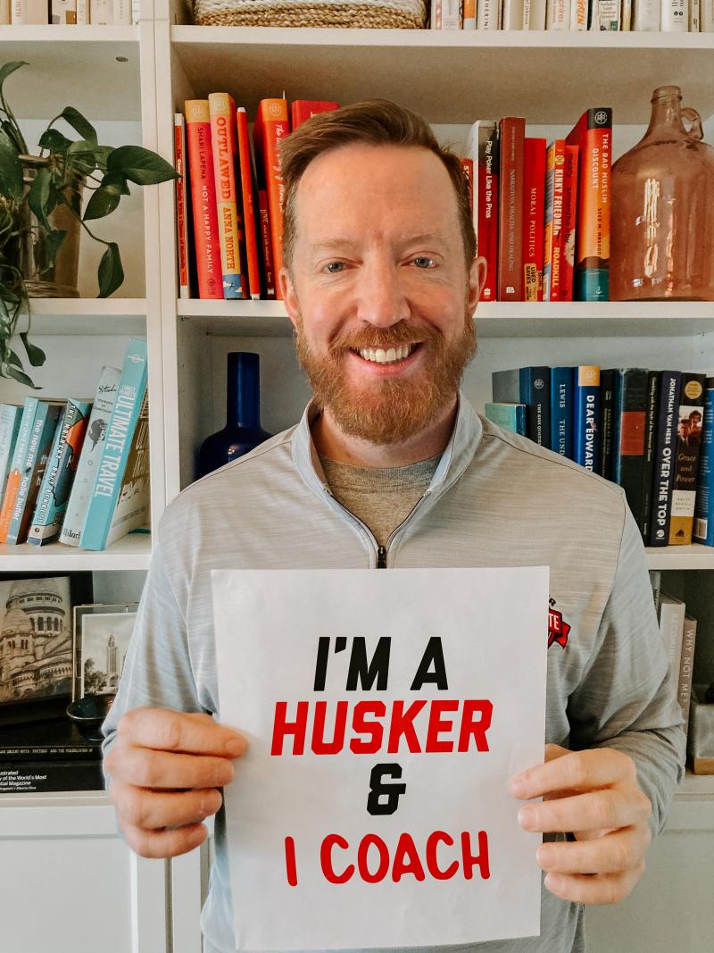 Aaron holds up a sign that says "I'm a Husker & I coach"