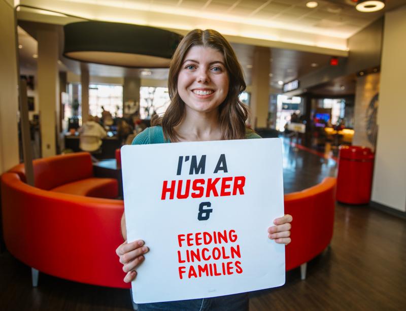 Hannah smiles for a photo with a sign that says “I’m a Husker & feeding Lincoln families”