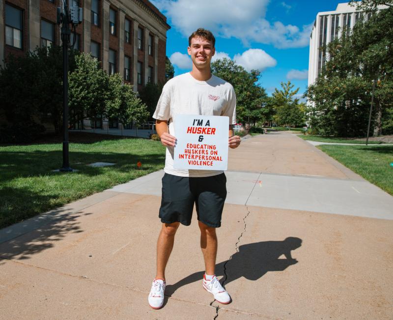 James holds a sign that says “I’m a Husker & educating Huskers on interpersonal violence”
