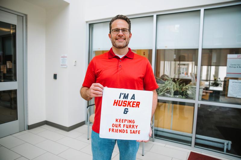Jeff smiles for a photo with a sign that reads "I'm a Husker & keeping our furry friends safe"