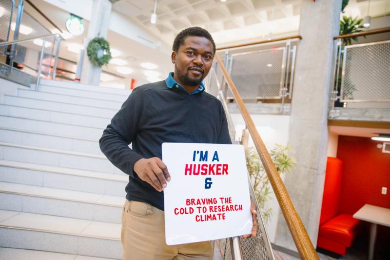 Jerome poses for a photo with a sign that says "I'm a Husker & Braving the Cold to Research Climate"