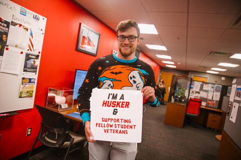 Kyle takes a photo in the Veteran Success Center holding a sign that says "I'm a Husker & supporting fellow student veterans"