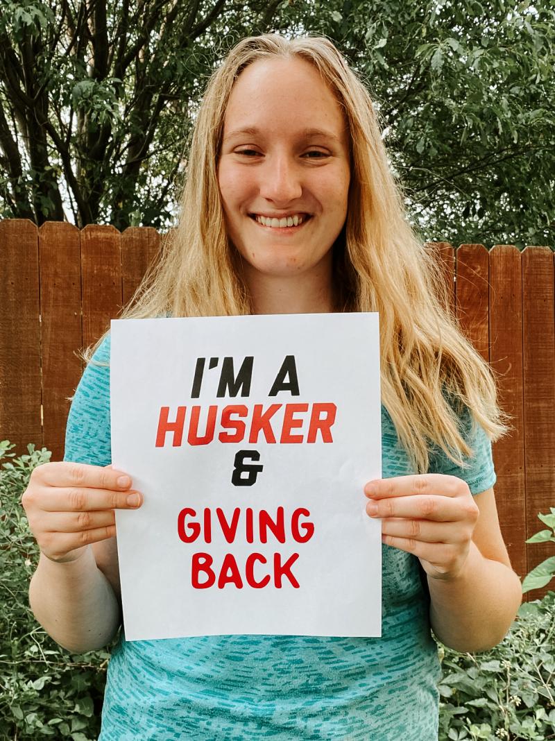 Lauren smiles as she holds a sign that says "I'm a Husker & giving back"