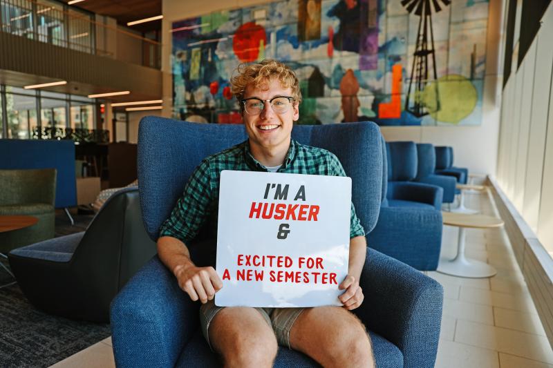 Paul smiles for a photo in Carolyn Pope Edwards Hall as he holds a sign that reads “I’m a Husker & excited for a new semester”