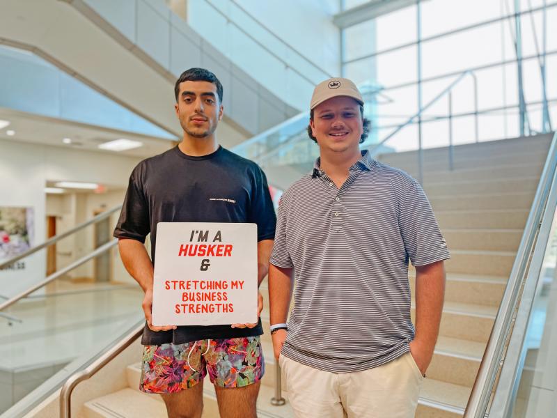 Rob Khorrom and Zach Molzer smile for a photo inside Hawks Hall with a sign that reads “I’m a Husker & stretching my business strengths”