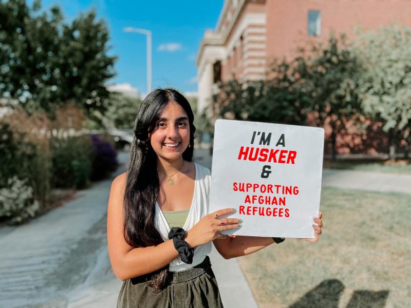Suzi smiles for a photo holding a sign that says "I'm a Husker & supporting Afghan refugees"