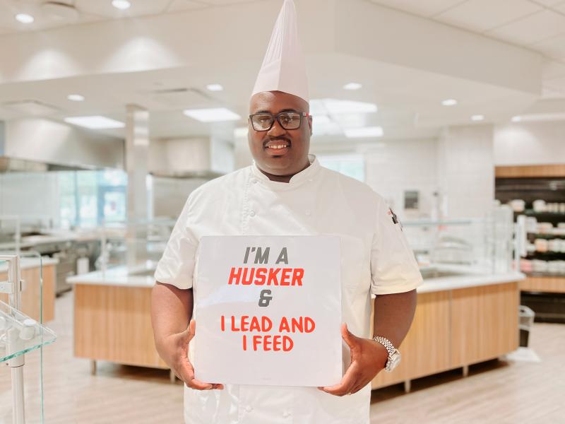 Wahadi Allen stands in the East Campus dining center and holds a sign that reads, "I'm a Husker & I lead and I feed"