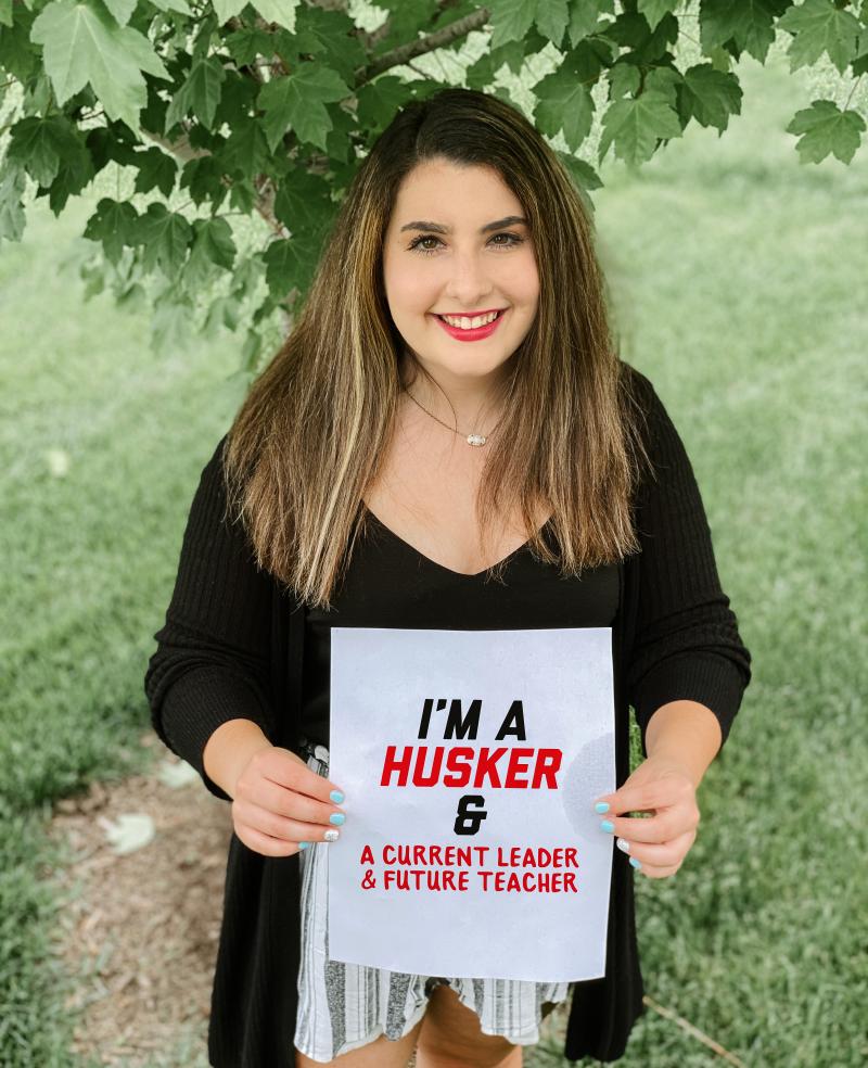 Julia holds a sign that says "I'm a Husker & a current leader & future teacher"