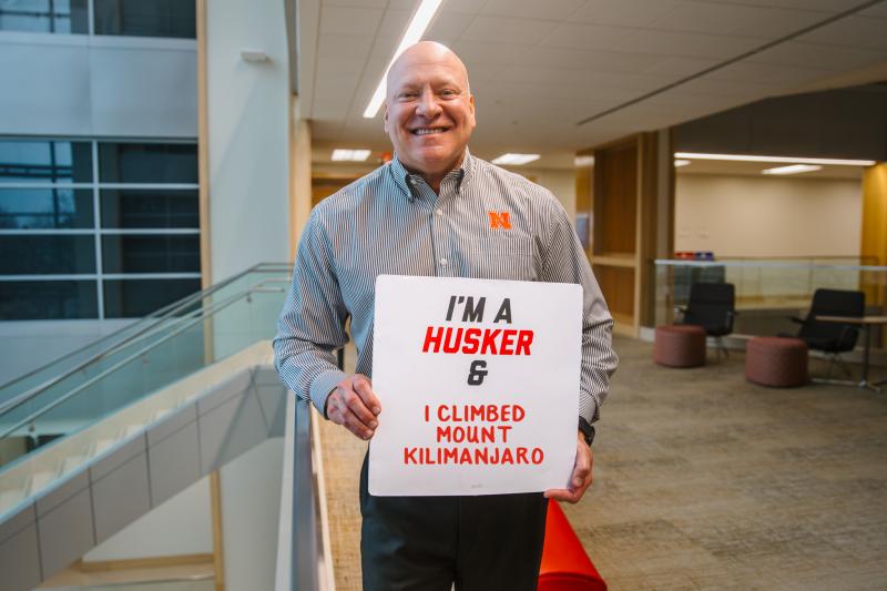 Kevin smiles for a photo with a board that says "I'm a Husker & I climbed Mount Kilimanjaro
