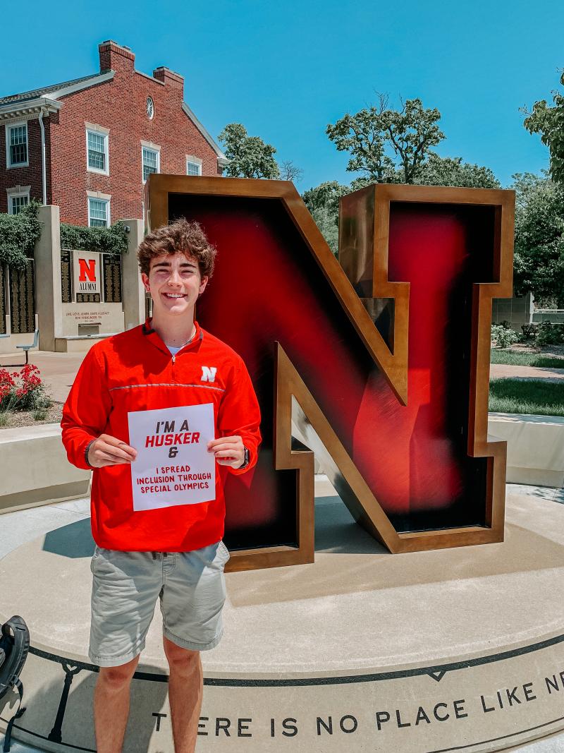 Nate smiles holding a sign that says “I’m a Husker & I spread inclusion through Special Olympics”