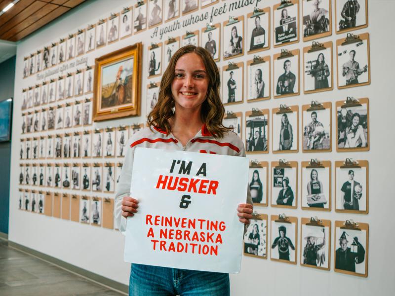 Alexa smiles for a photo outside the Engler space on East Campus. She holds a sign that says “I’m a Husker & reinventing a Nebraska tradition”