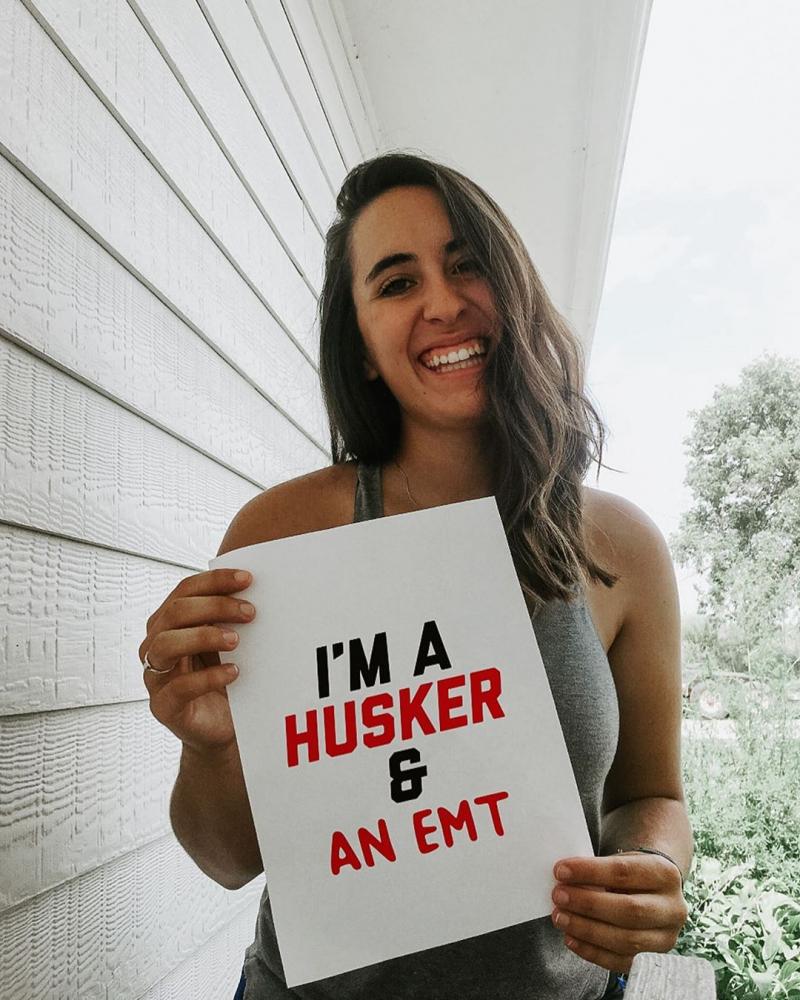 Kelsey holding a sign that says "I'm a Husker and an EMT."