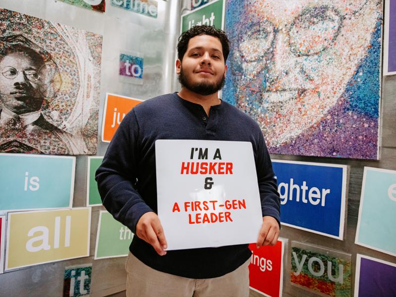Greg poses for a photo holding a sign that says "I'm a Husker & a first-gen leader"