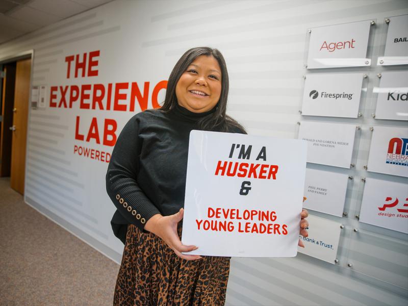 Jemalyn smiles for a photo in the Experience Lab holding a sign that says “I’m a Husker and developing young leaders”