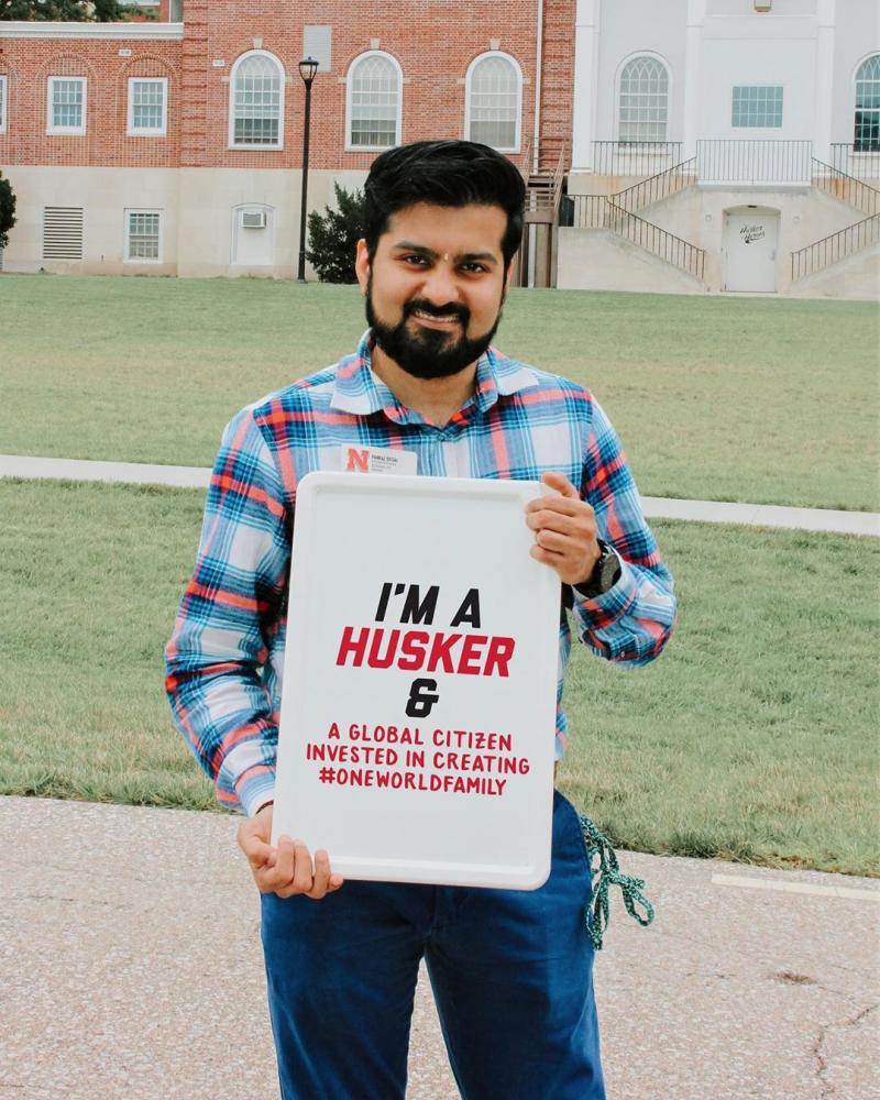 Pankaj holding a sign that says "I'm a Husker and a global citizen invested in creating #OneWorldFamily."."
